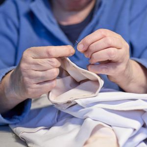 Detailed view of hands sewing fabric, showcasing craftsmanship and skill in the tailoring process.